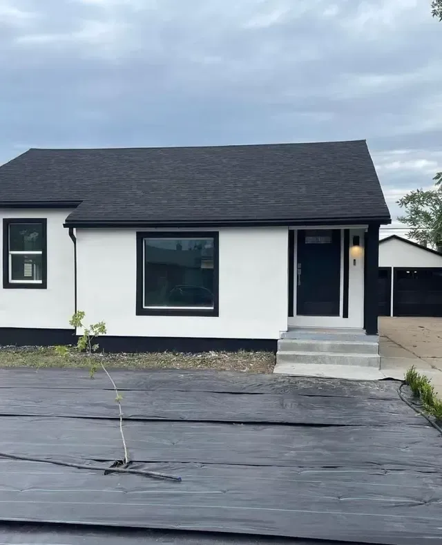 A white house with a black roof and a black driveway.
