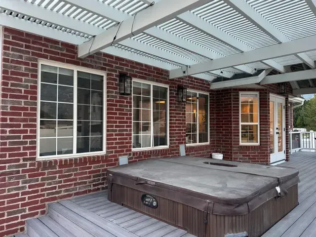 There is a hot tub on the deck of a brick house.