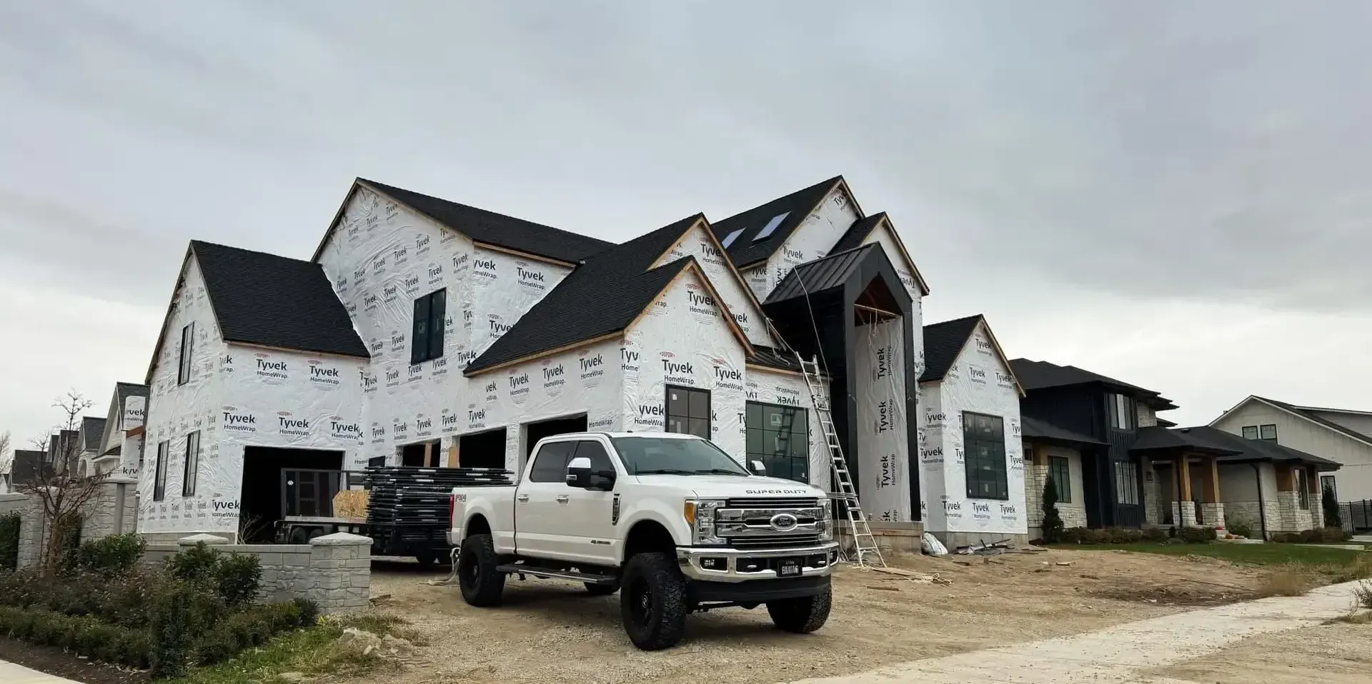 A white truck is parked in front of a large house under construction.