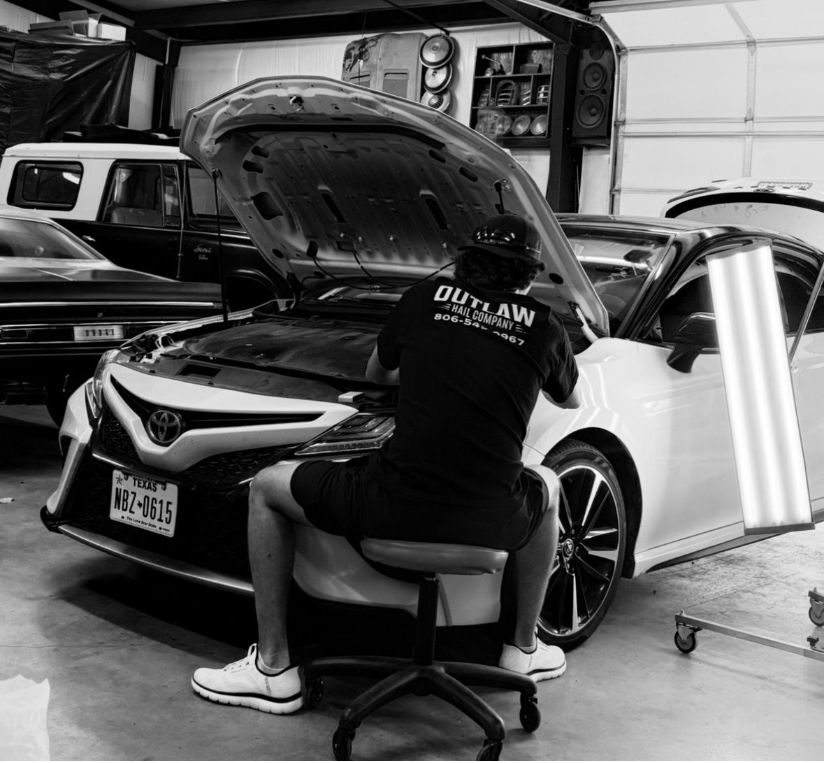 Mechanic working on a white car in a garage with hood up.
