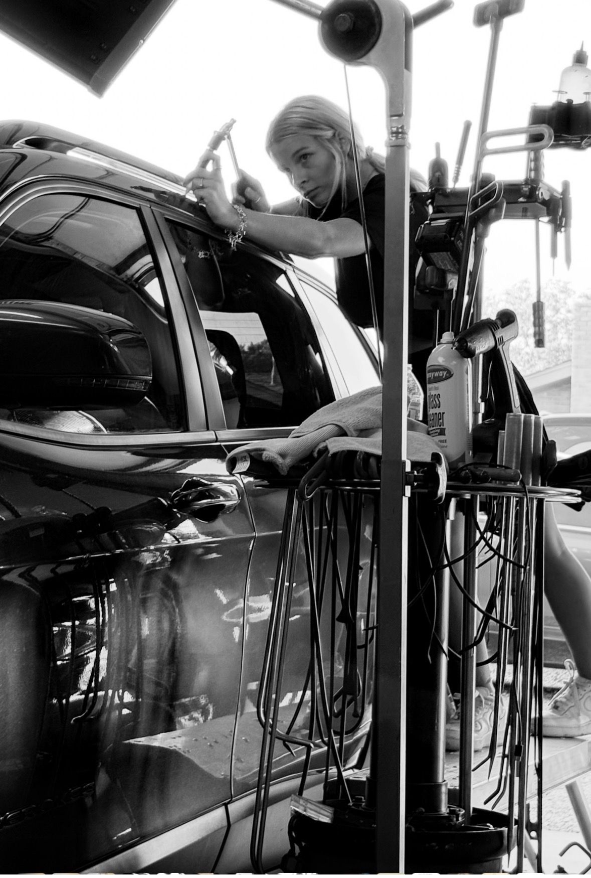 Woman repairing a car dent, using tools next to the black vehicle.