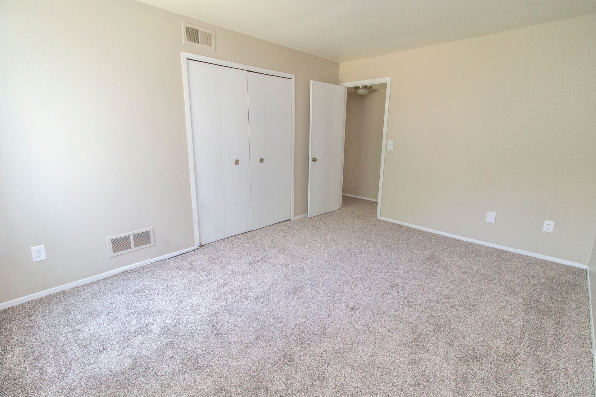 An empty bedroom with a carpeted floor and two closets.