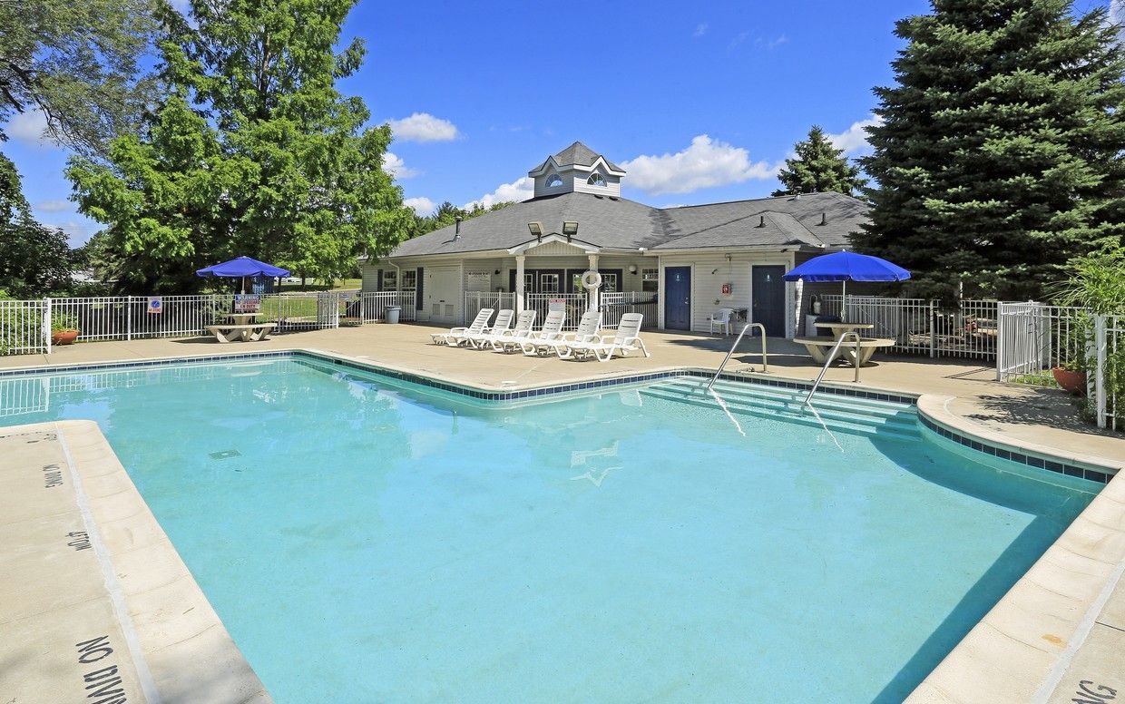 A large swimming pool is surrounded by chairs and umbrellas in front of a house.