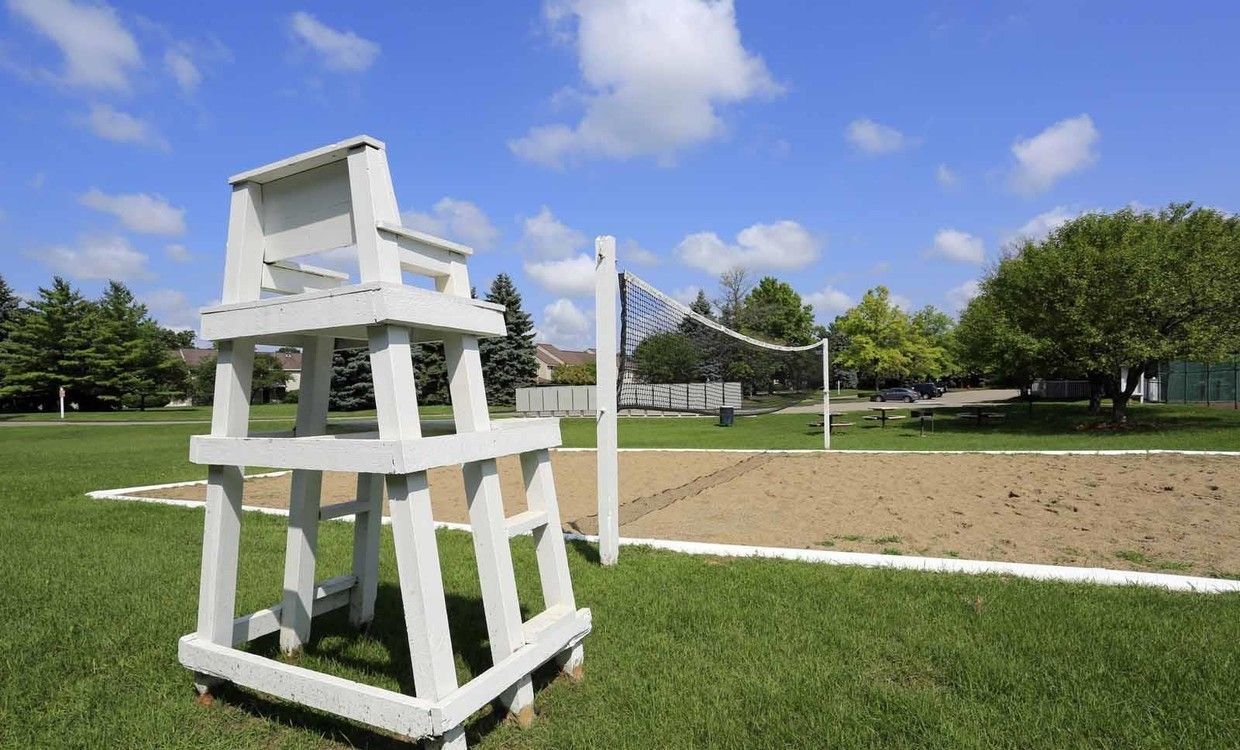 A lifeguard tower is sitting next to a volleyball net in a park.