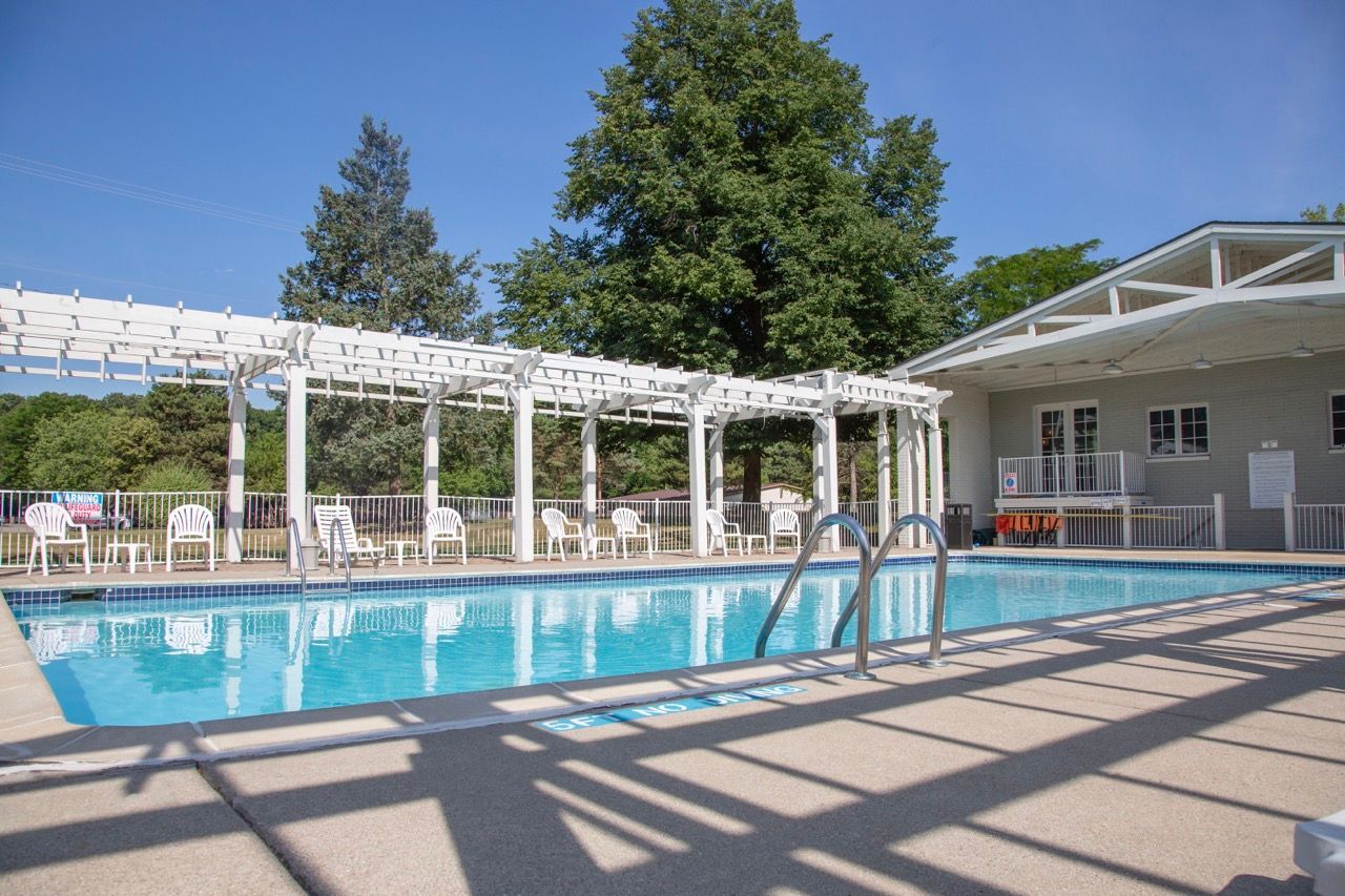 A large swimming pool with a pergola and chairs around it.