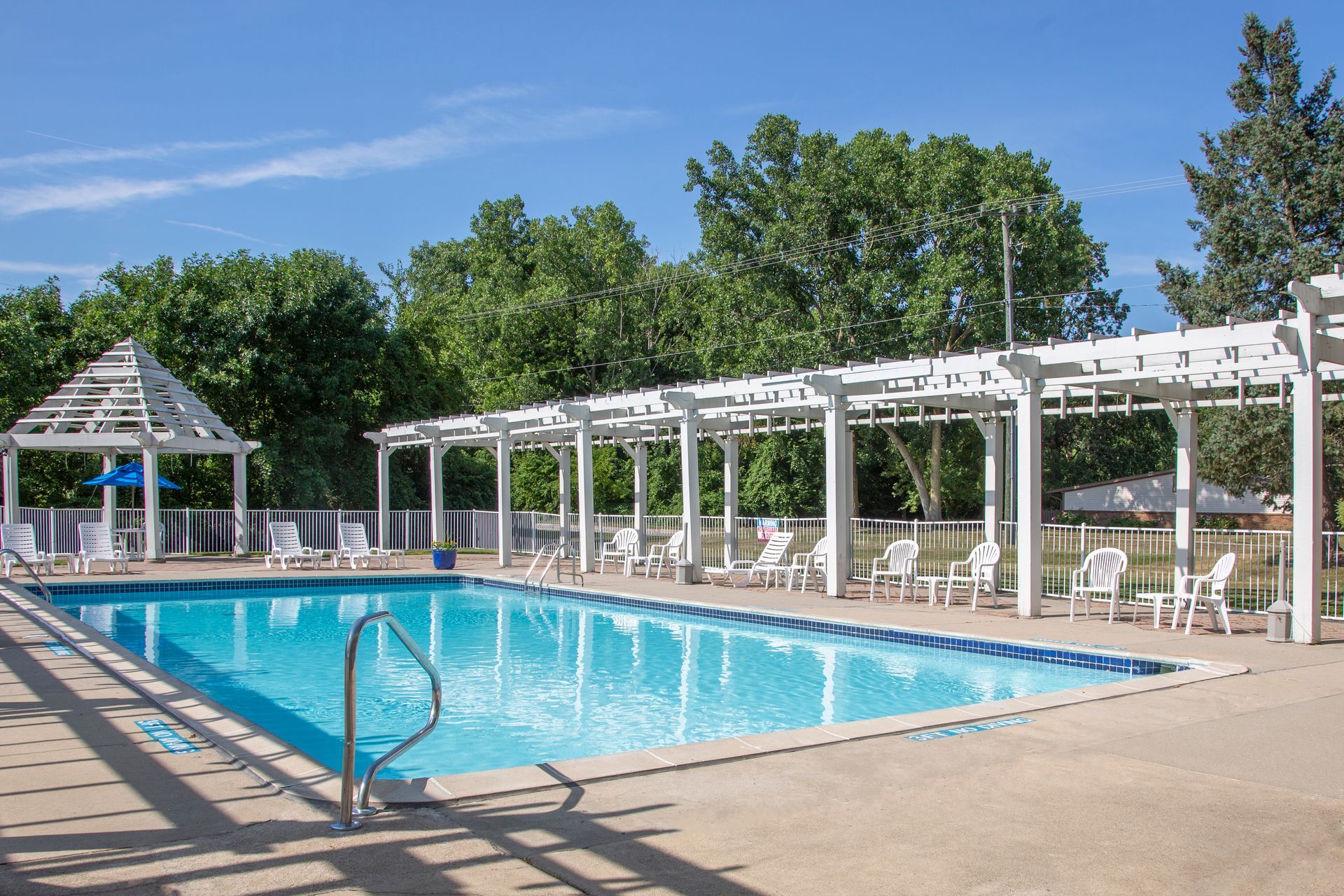 A large swimming pool with a gazebo and chairs around it