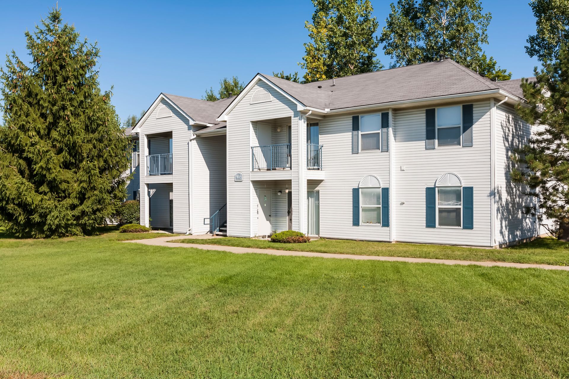 A white apartment building with blue shutters and a lush green lawn in front of it.