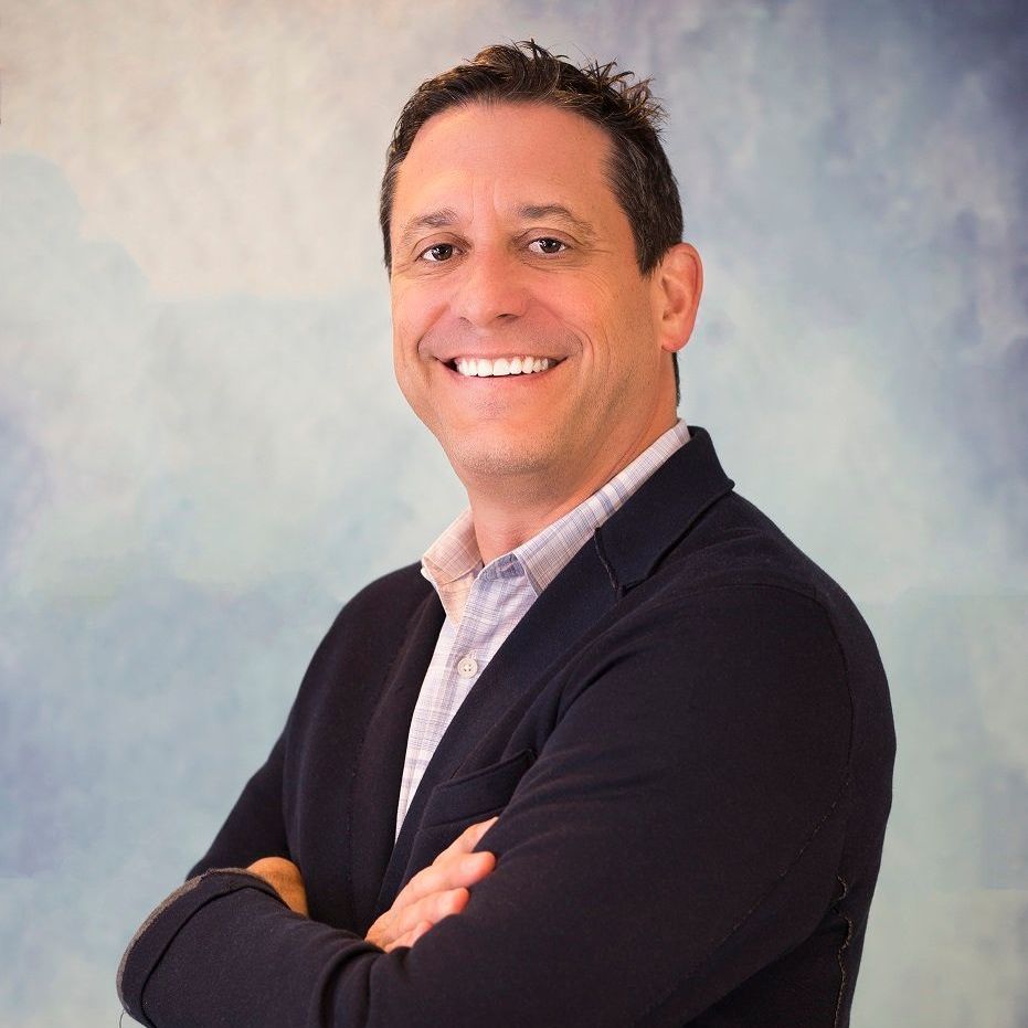 DAVID JACOBSON in a suit is smiling with his arms crossed.