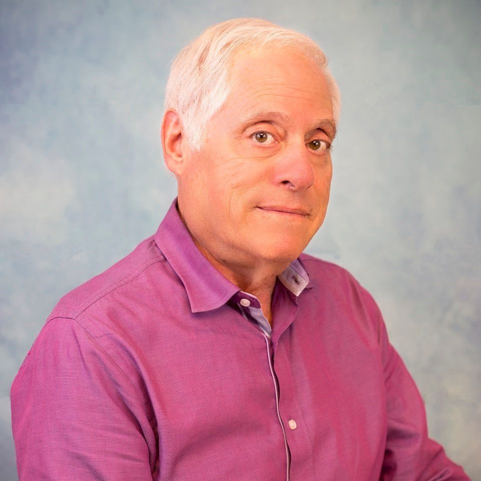 GARY ROSENTHAL in a suit is smiling with his arms crossed.