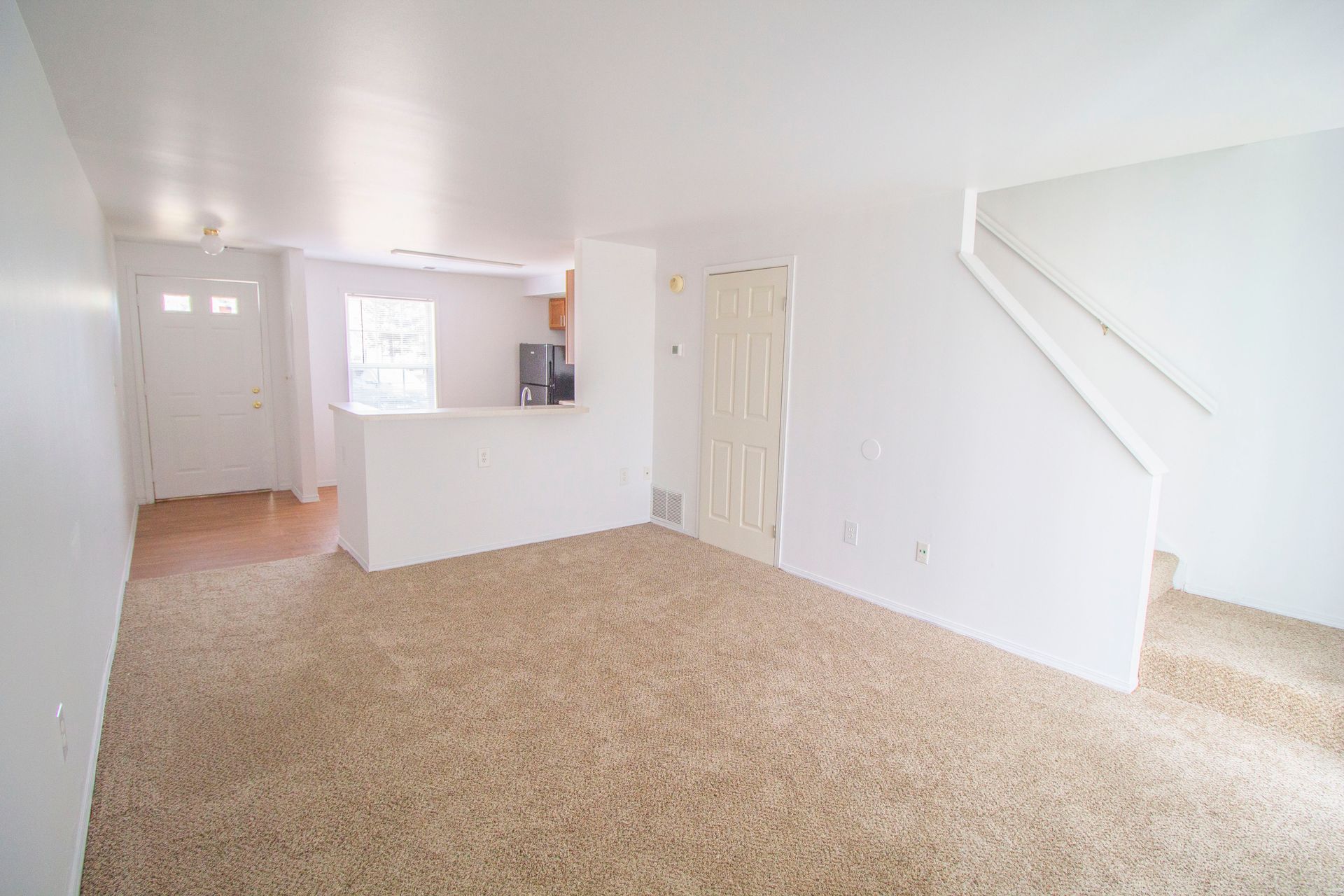 An empty living room with a carpeted floor and white walls.