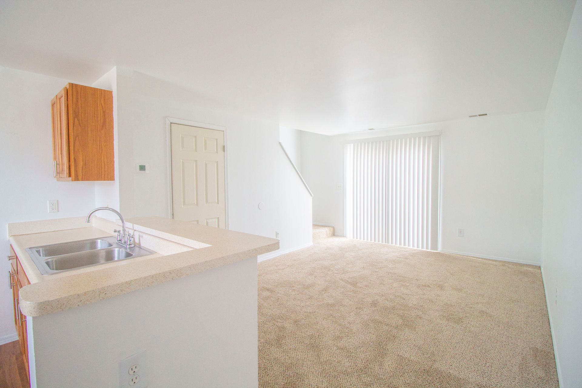 An empty apartment with a kitchen , living room , and stairs.