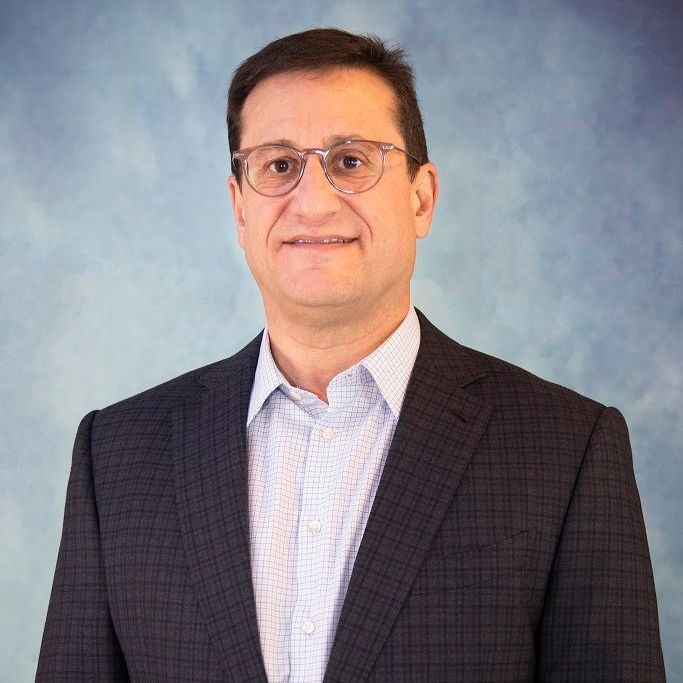 HOWARD JACOBSON in a suit is smiling with his arms crossed.