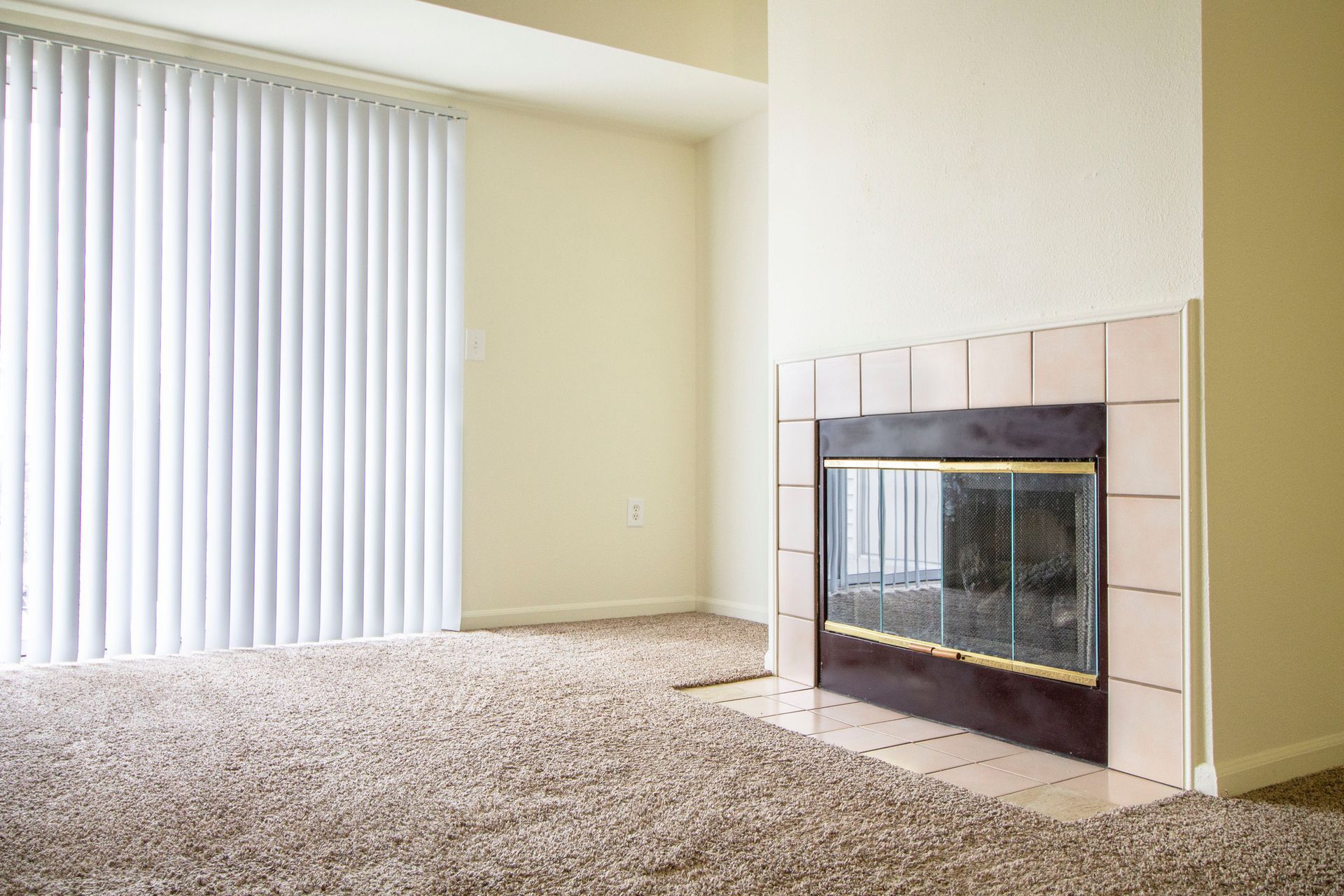 An empty living room with a fireplace and blinds.