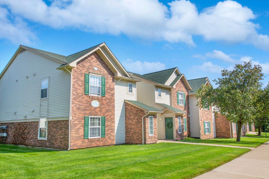 A row of apartment buildings with green shutters and a lush green lawn.
