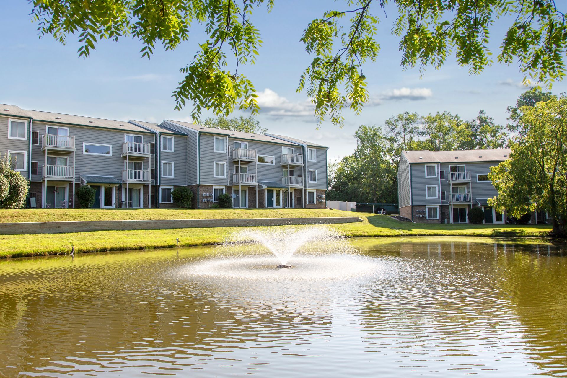 A pond with a fountain in the middle of it in front of a building.