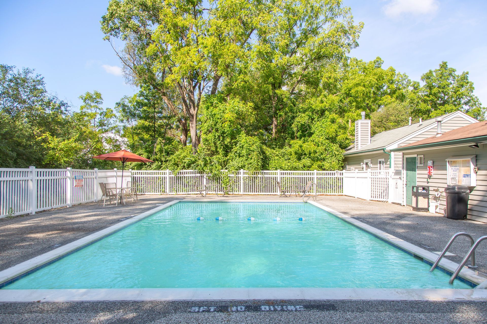 A large swimming pool surrounded by trees and a white fence.