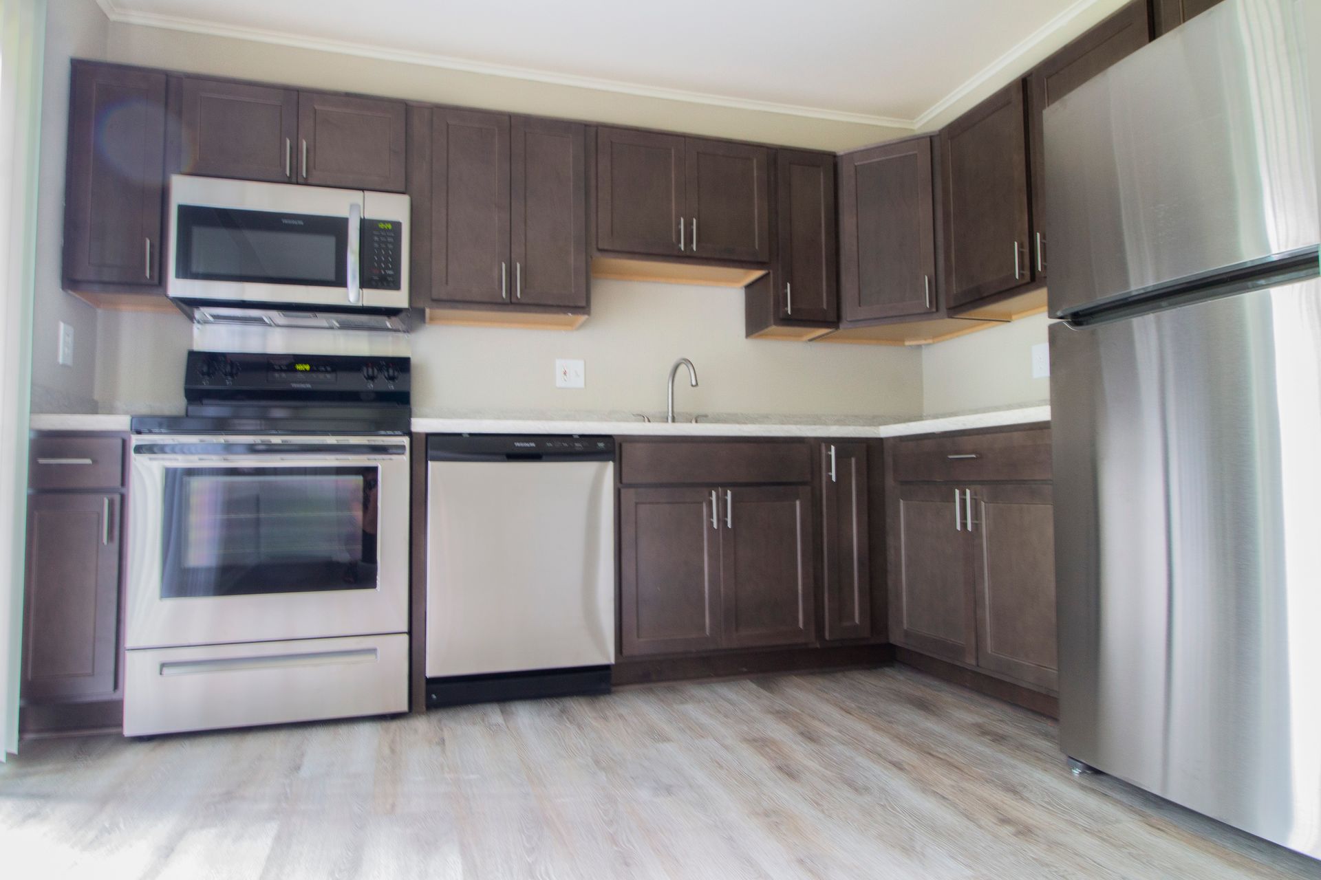 An empty kitchen with stainless steel appliances and wooden cabinets.