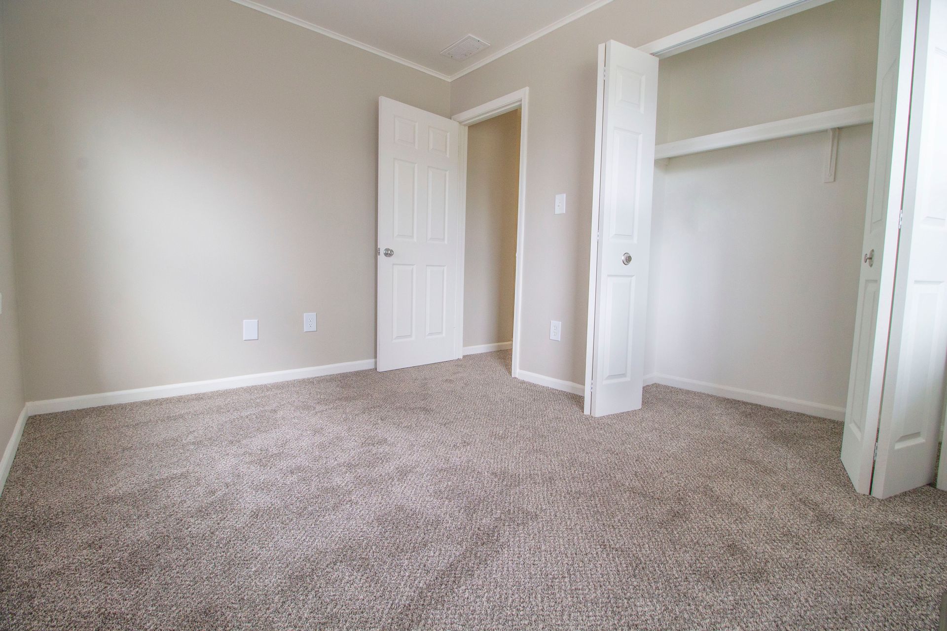 An empty bedroom with a carpeted floor and a closet.