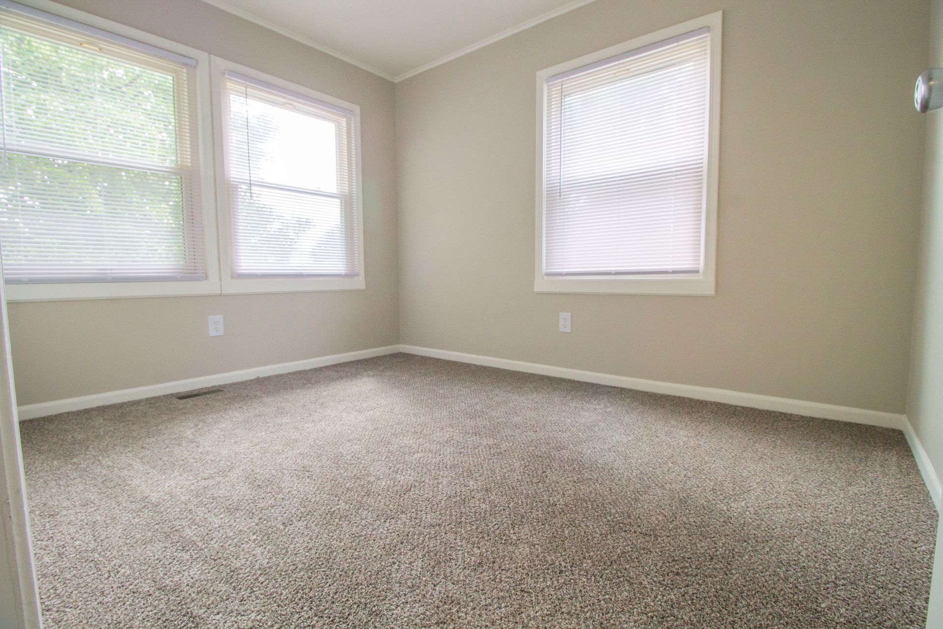 An empty room with a carpeted floor and two windows.