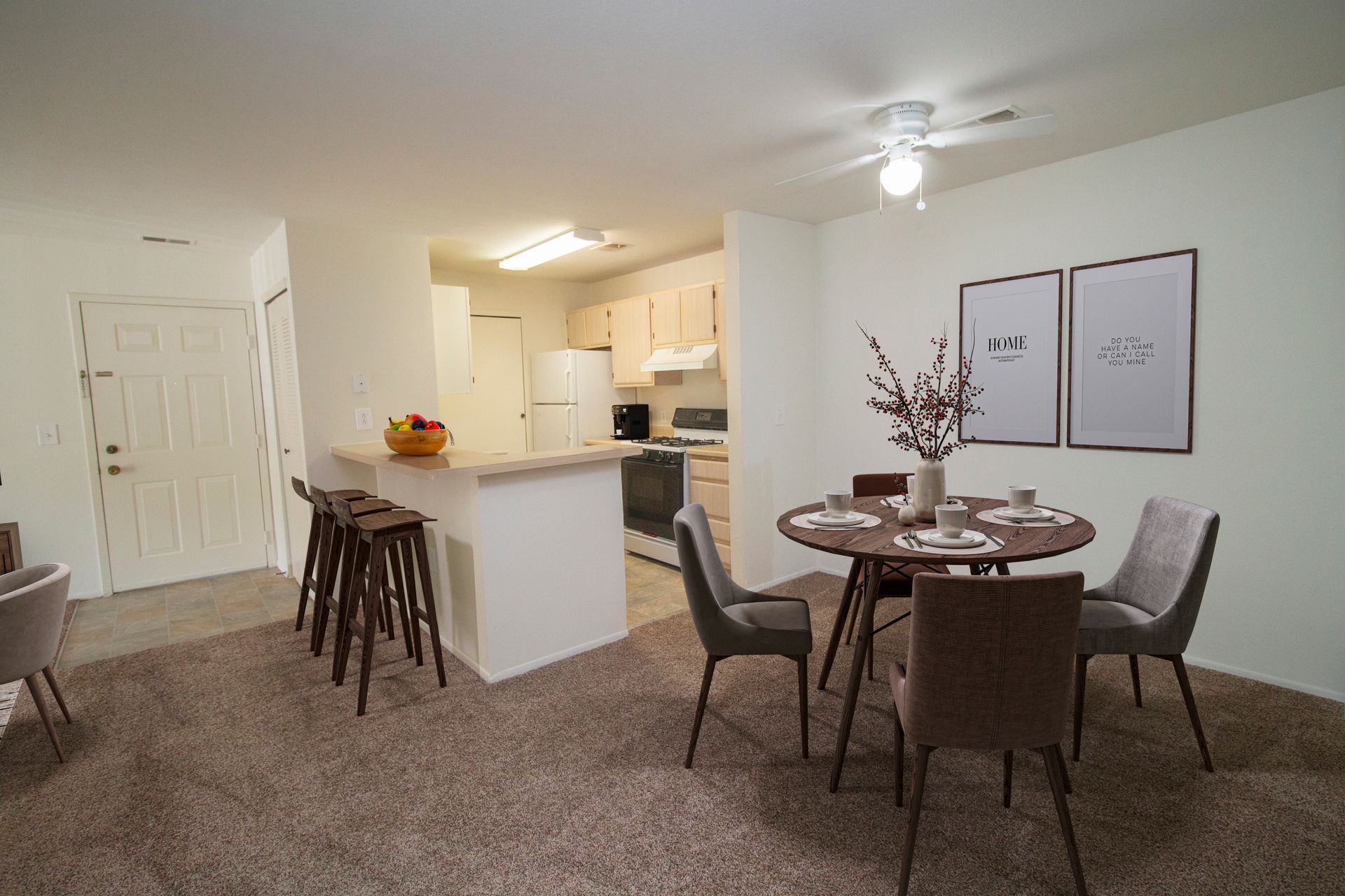 A dining room with a table and chairs and a kitchen in the background.