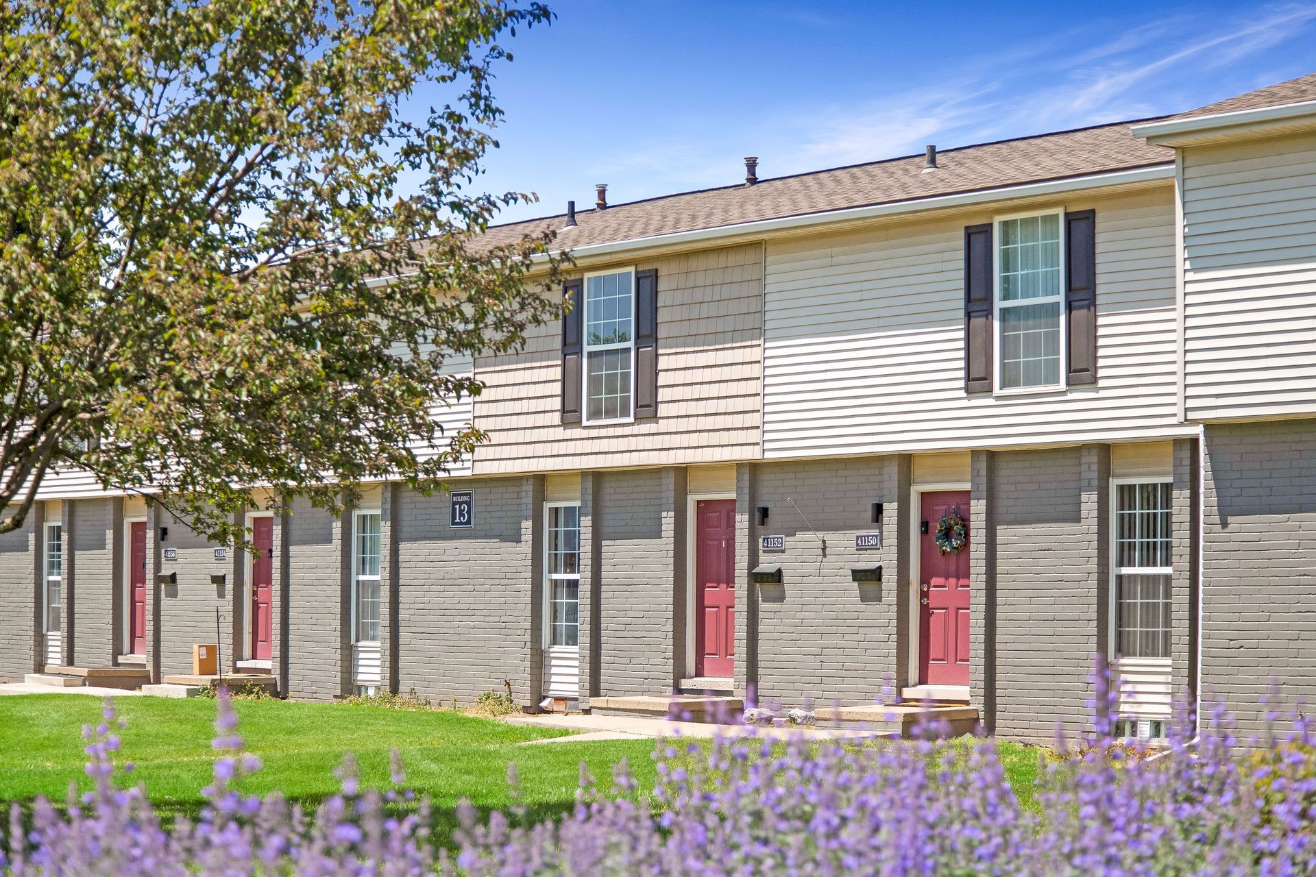 A row of apartment buildings with red doors and purple flowers in front of them.