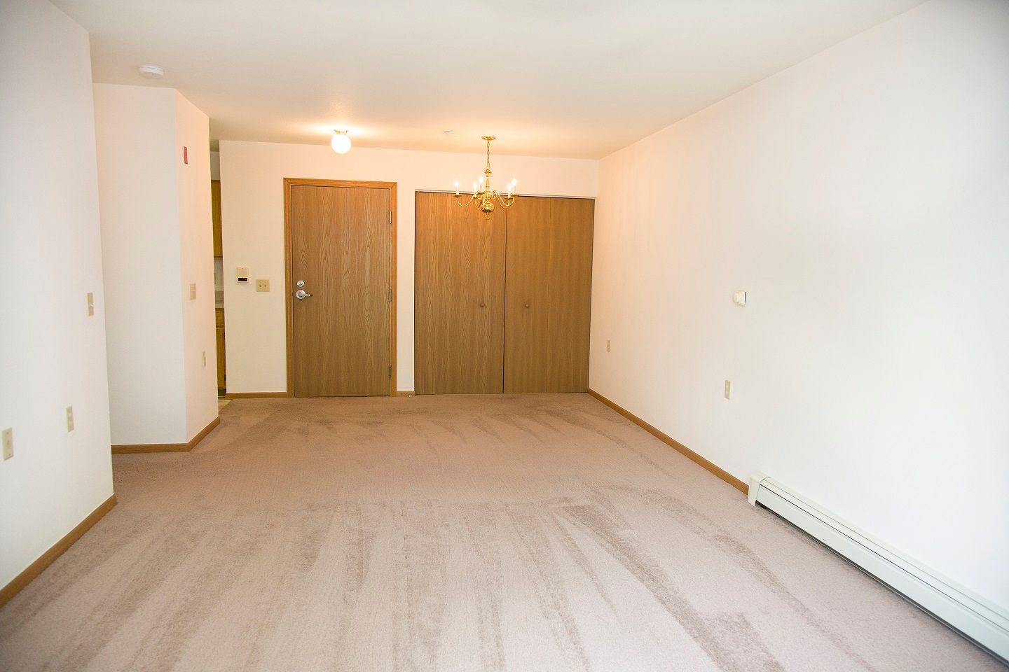 An empty living room with two doors and a chandelier
