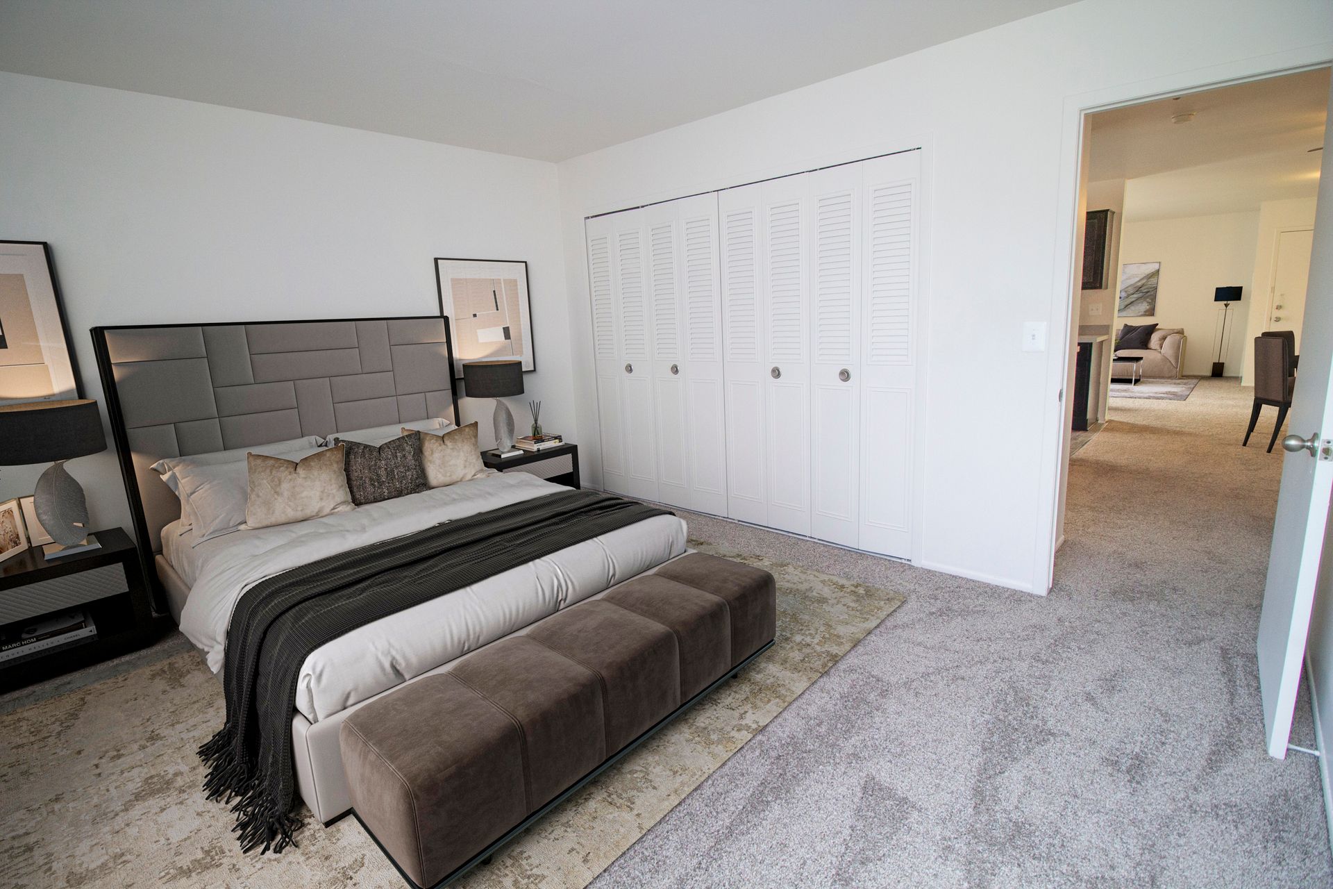 A bedroom with a large bed , ottoman , nightstands , and closets.