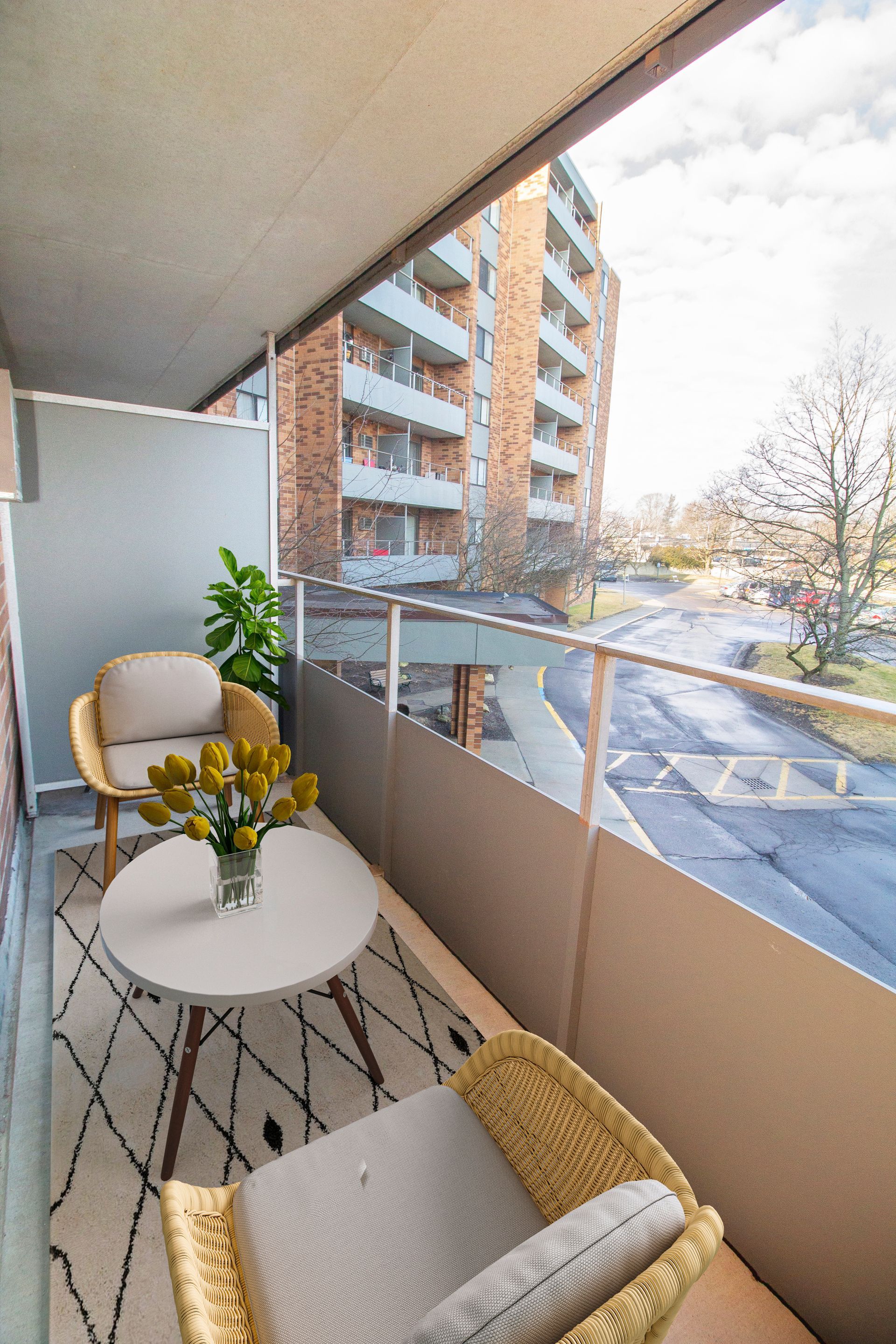 A balcony with chairs , a table and a vase of flowers.