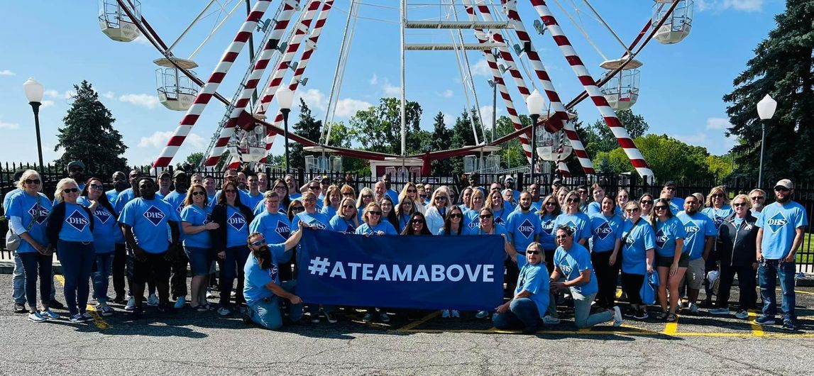 A large group of people are posing for a picture in front of a ferris wheel.