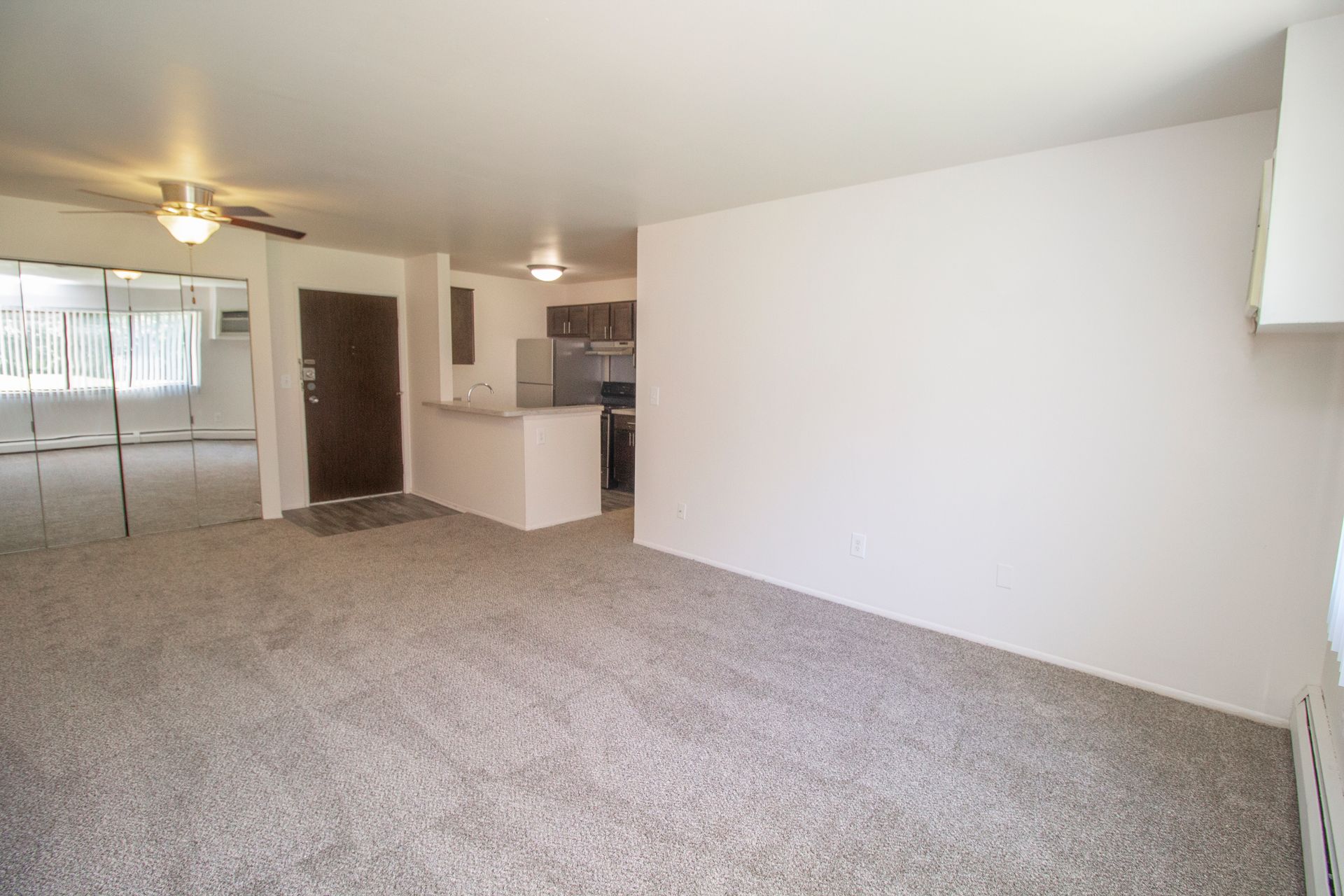 An empty living room with a ceiling fan and a mirror.