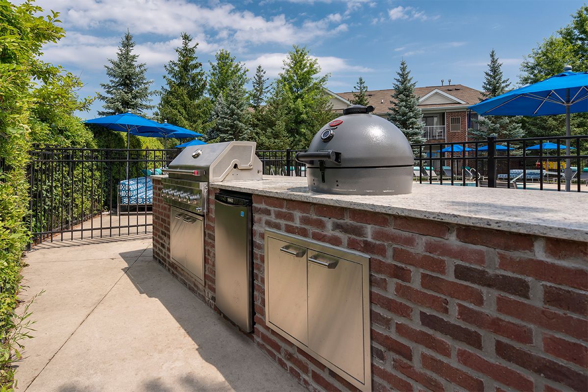 A grill is sitting on top of a brick wall next to a pool.