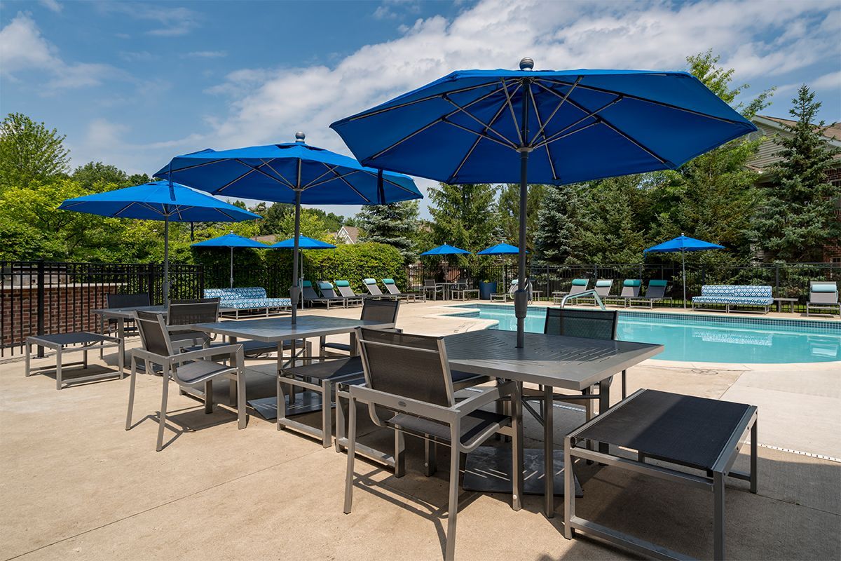 A swimming pool with tables and chairs and blue umbrellas