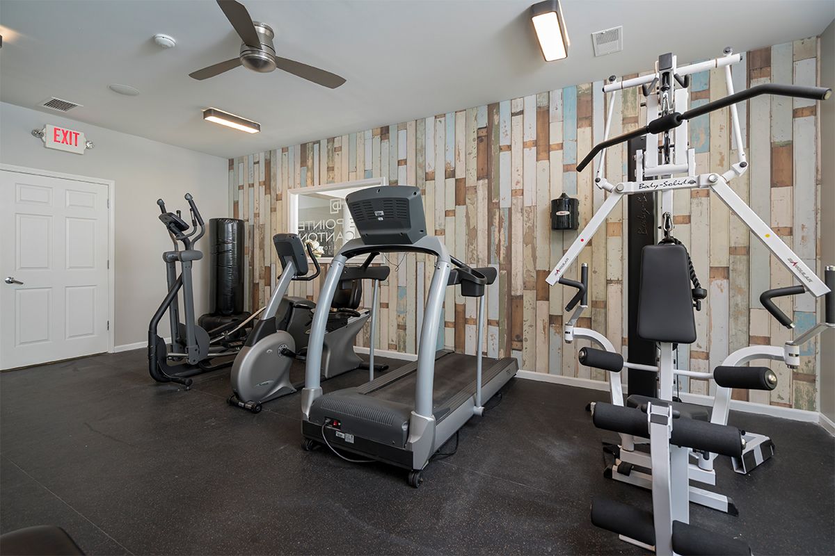 A gym with treadmills , exercise bikes , and a ceiling fan.
