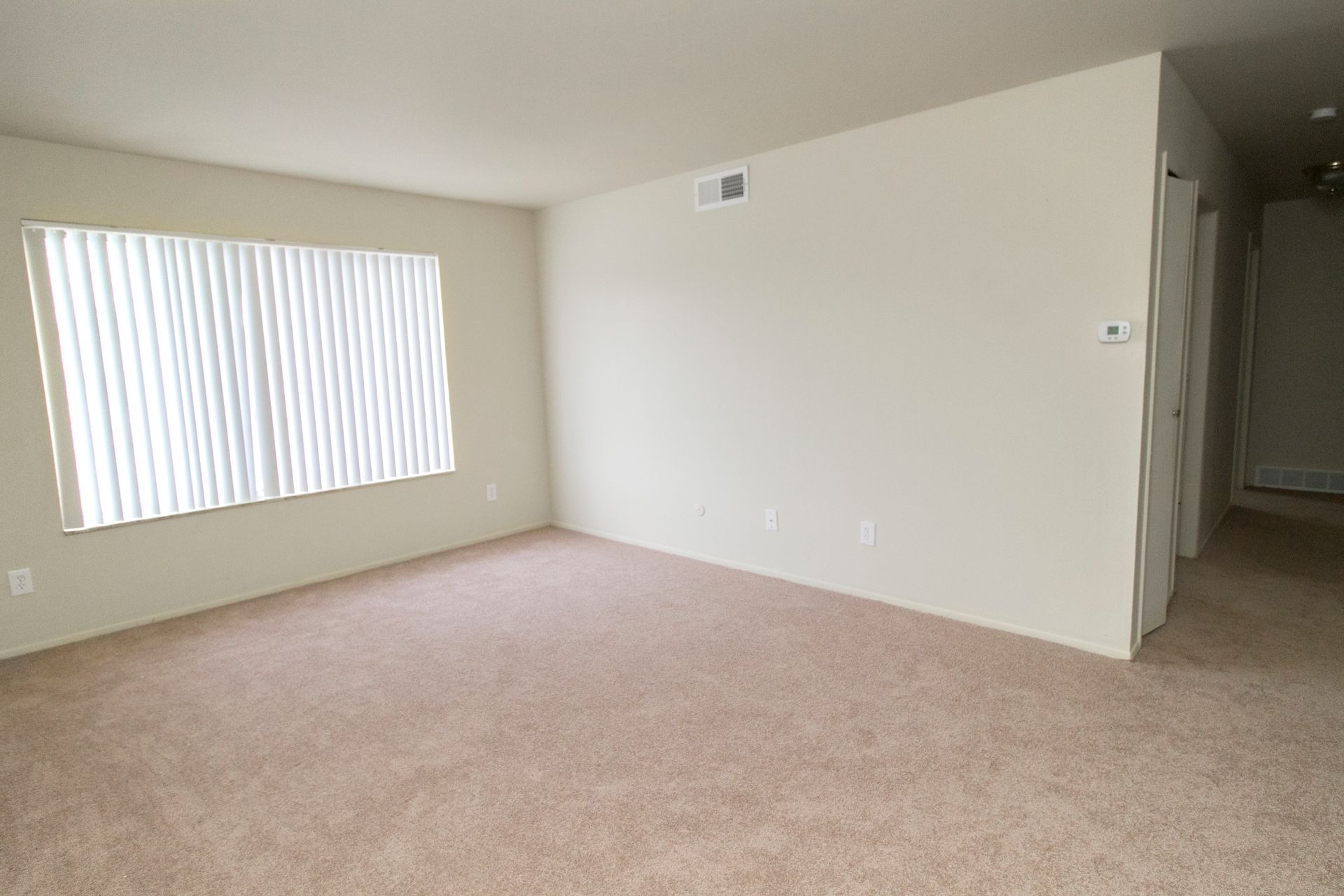 An empty living room with a large window and a carpeted floor.