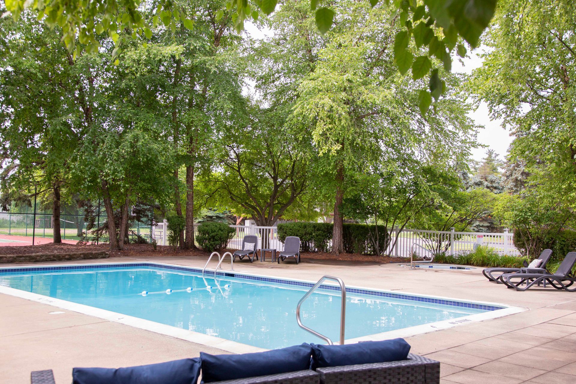 A large swimming pool is surrounded by trees and chairs.