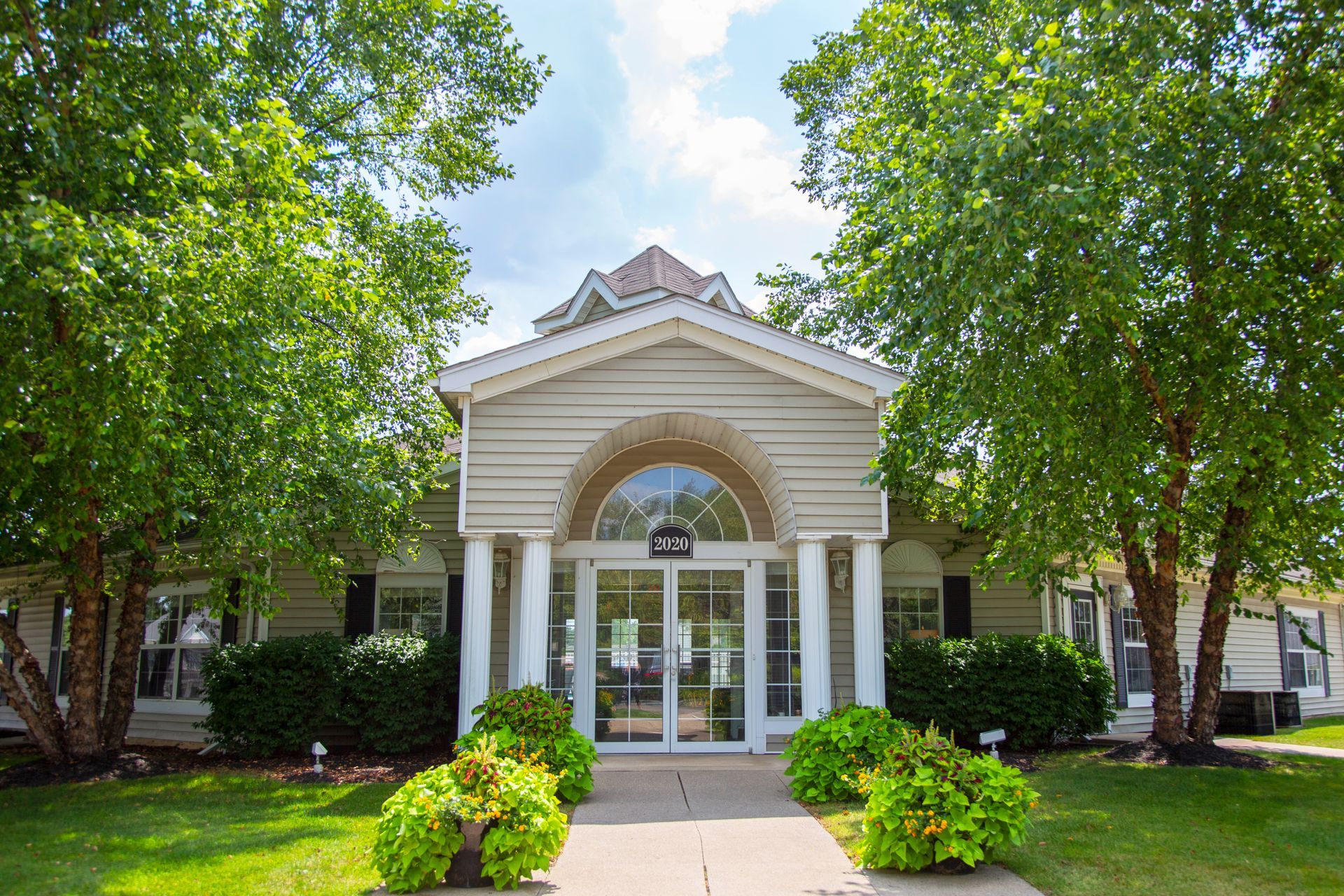 A large white building with a walkway leading to it is surrounded by trees.