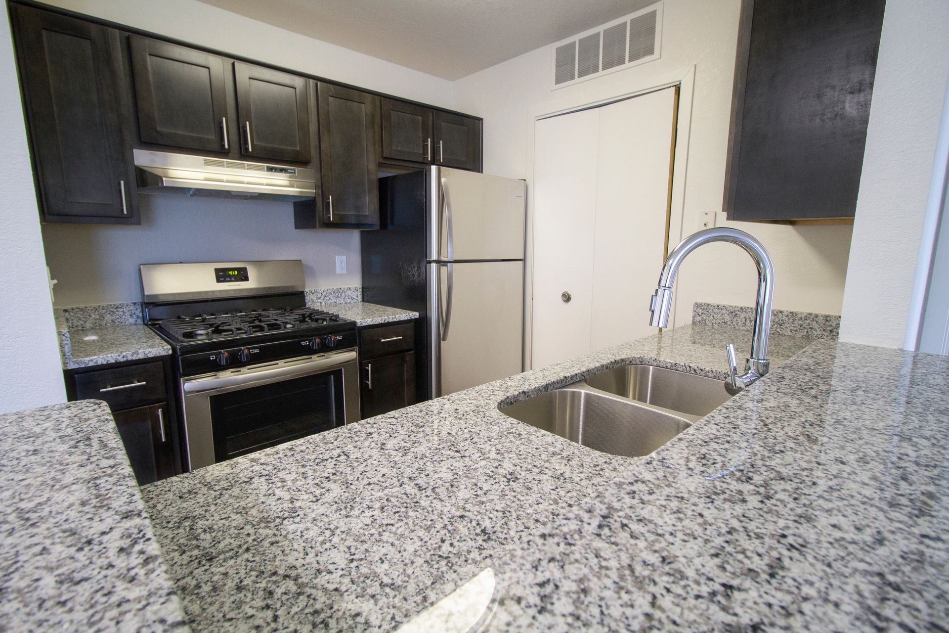 A kitchen with granite counter tops , black cabinets , a sink and a dishwasher.