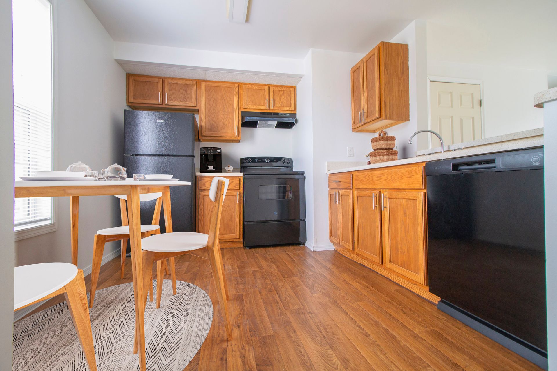 A kitchen with wooden cabinets , a black refrigerator , a stove , a table and chairs.