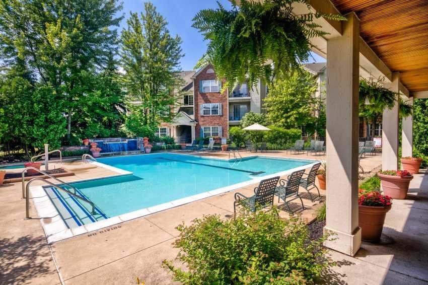 A large swimming pool is surrounded by chairs and plants in front of a building.