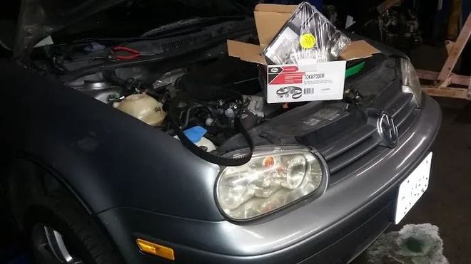 A car with the hood up and a box on the hood.