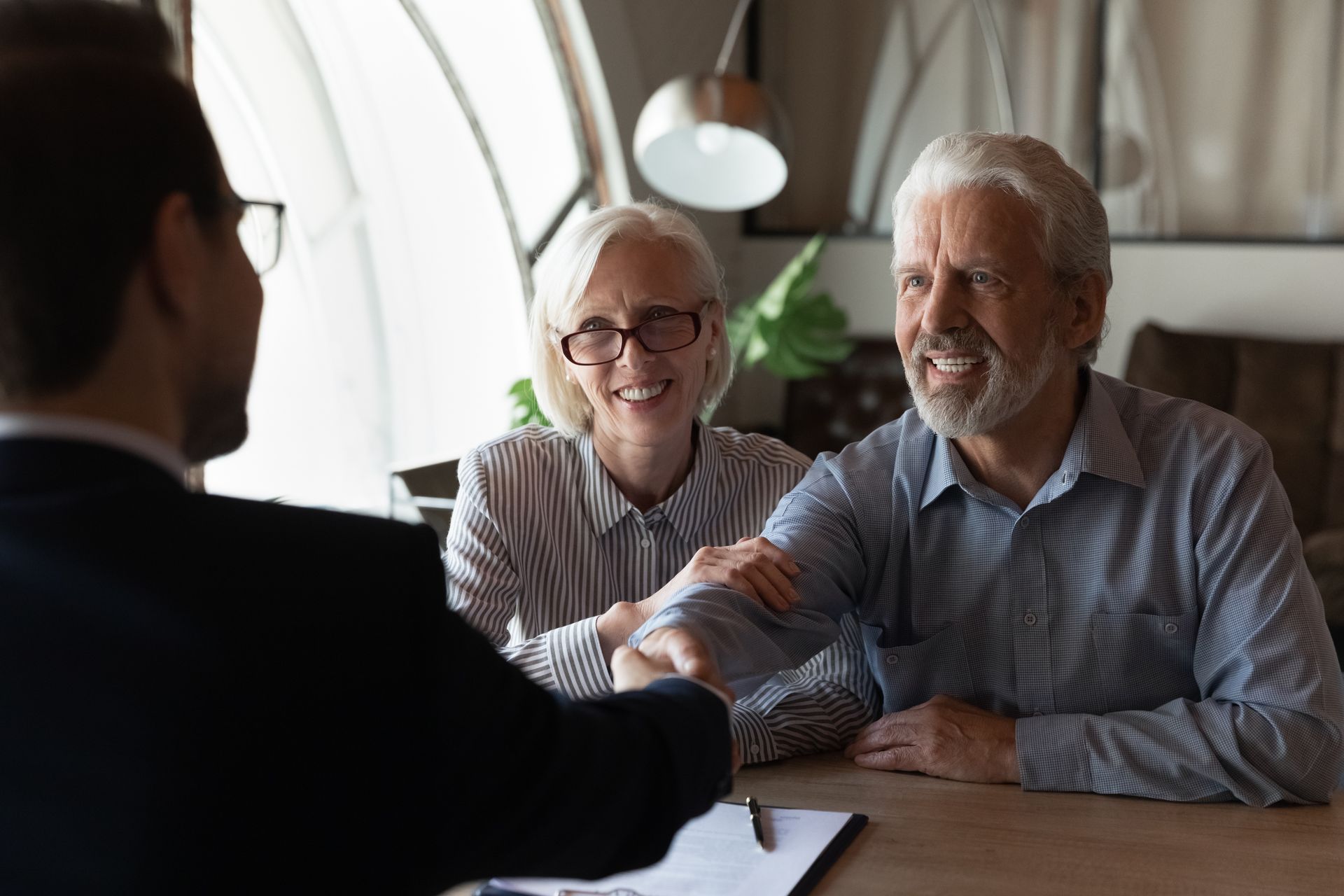 Smiling senior couple shaking hands with their attorney at a consultation meeting.