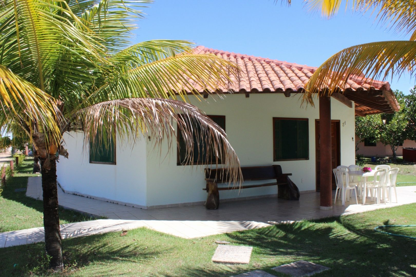 Uma casa branca com telhado de telha vermelha é cercada por palmeiras