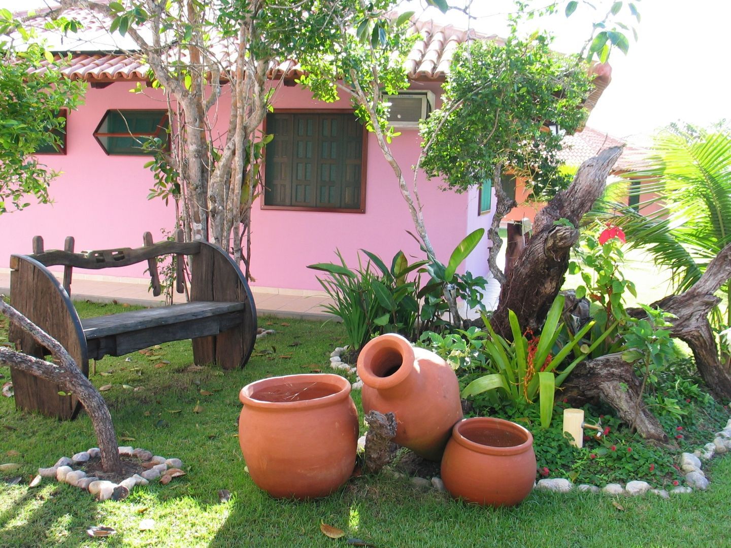 Um jardim com vasos e um banco em frente a uma casa rosa