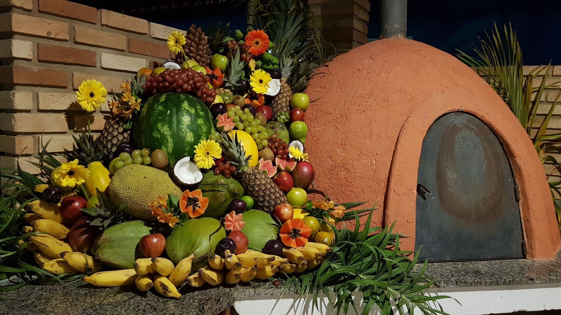 Um monte de frutas e flores estão em frente a um forno.
