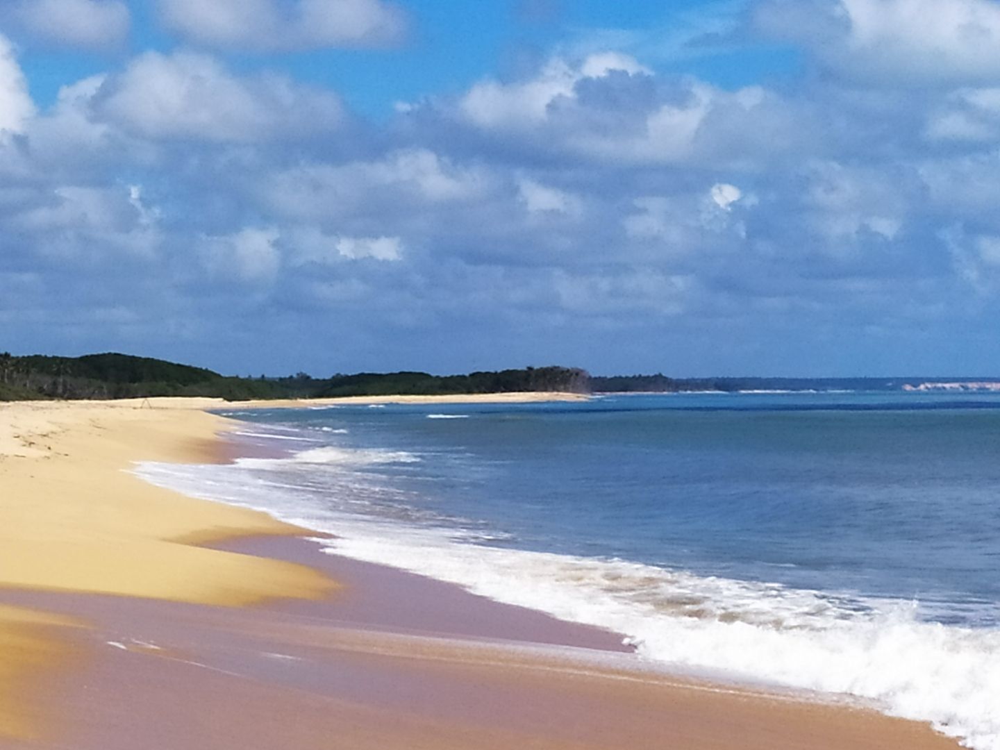 Uma praia de areia com ondas chegando em um dia ensolarado