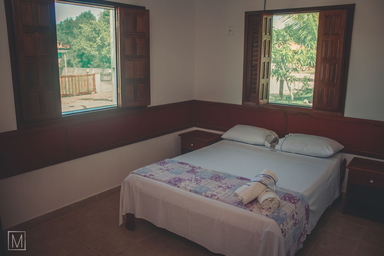 Um quarto com uma cama e duas janelas com persianas.