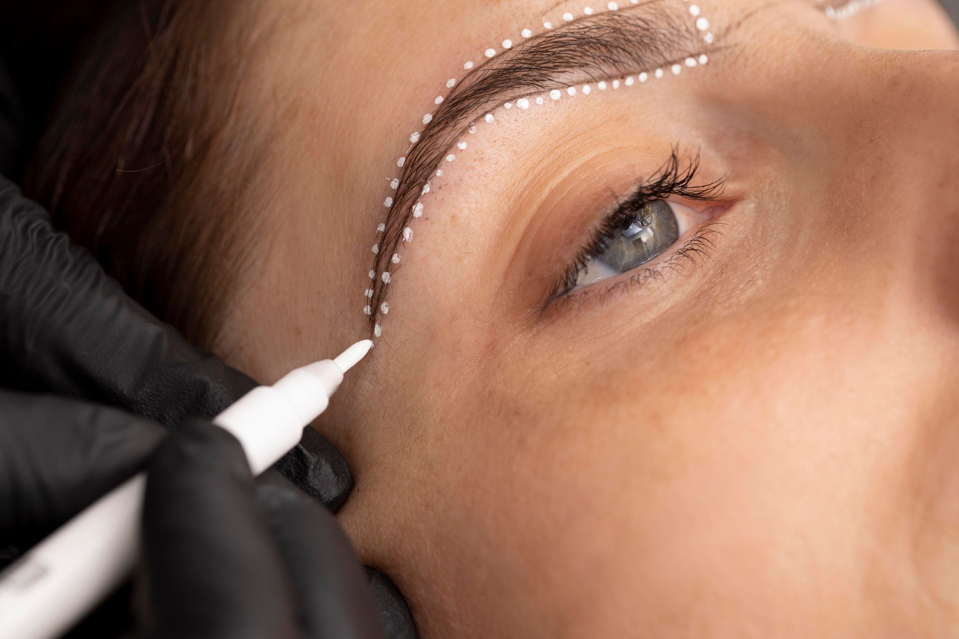 A woman is getting her eyebrows drawn by a tattoo artist.