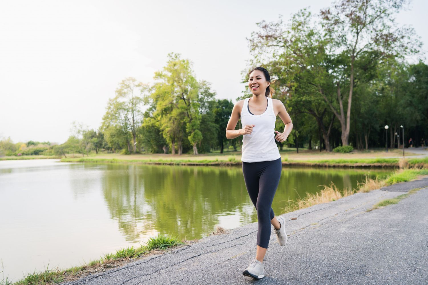 A woman is running by a lake in a park.