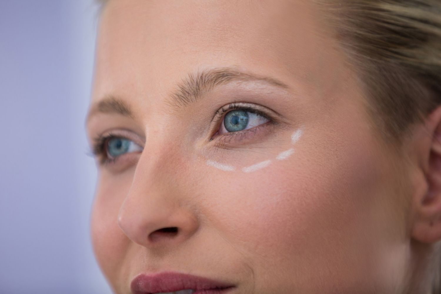 A close up of a woman applying eye cream to her eye.