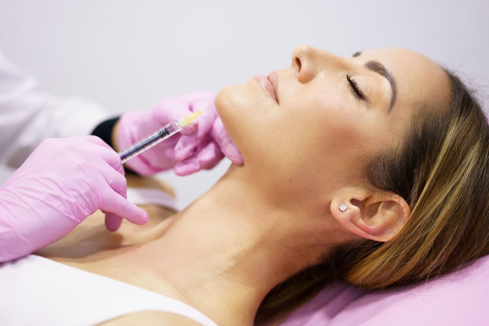 Woman receiving a neck injection from a gloved hand in a medical setting.